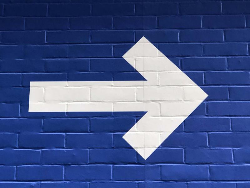 A white arrow painted on a blue brick wall