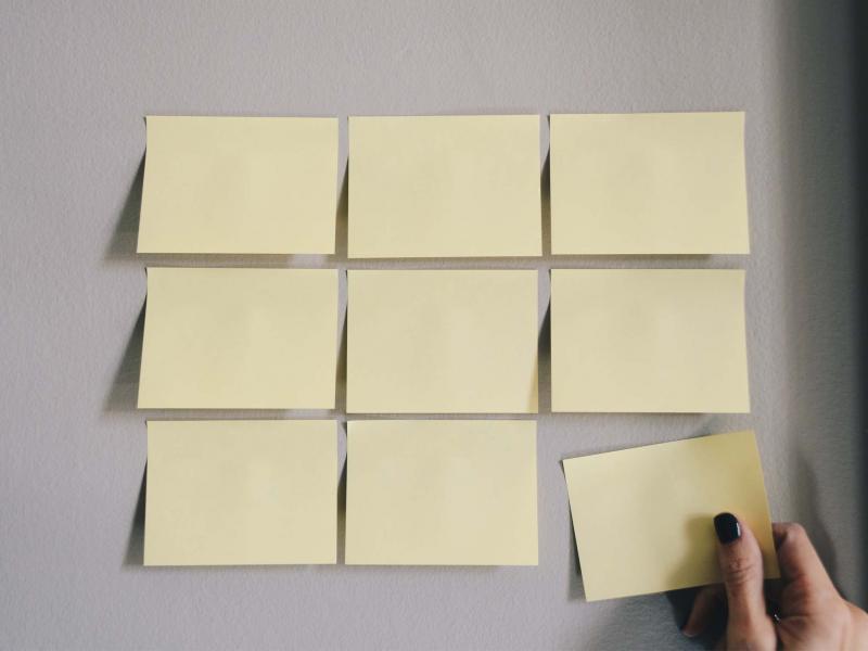9 post-it notes are lined up in a grid on a wall and a hand is tearing away the final post-it note on the bottom right corner